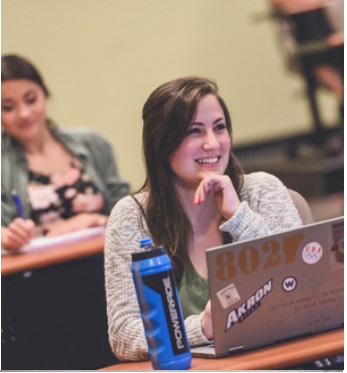 College of Business student sitting in a classroom with her laptop and waterbottle.