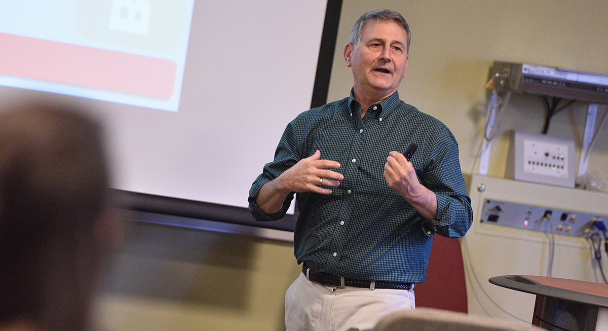 A professor lectures in front of a screen